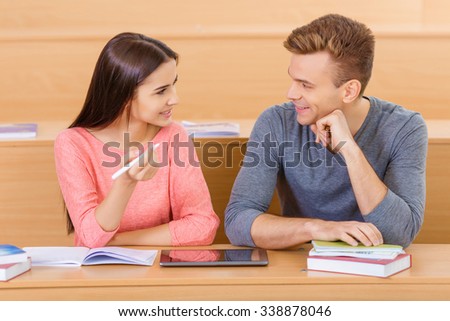 Classroom conversation. Nice-looking young girl is discussing the subject with her handsome fellow mate at the desk.