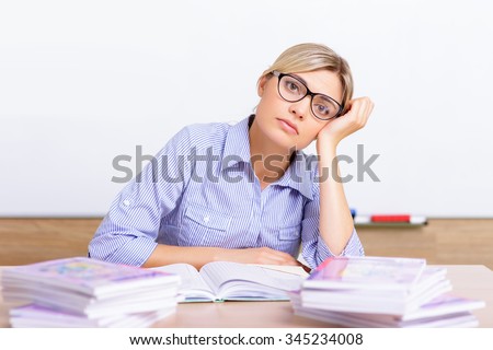 Pile of paperwork. Young nice-looking female teacher looks worried about enormous amount of work she has to complete.