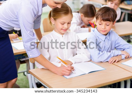 Lesson at school. Teacher leans down to help little girl to complete the task.
