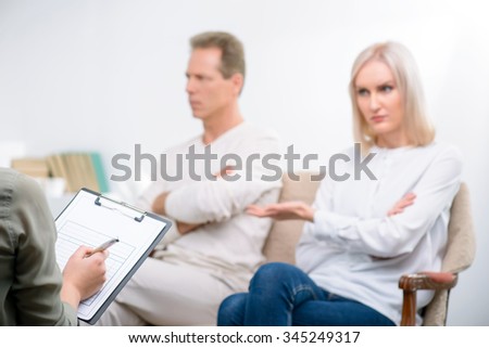 Can not live together. Selective focus of folder in hands of professional psychologist holding it and interrogating adult couple sitting on the sofa in the background