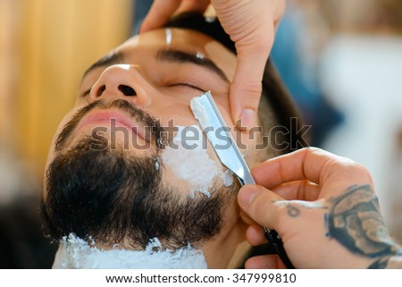 Crafty master. Close up of open razor in hands of professional barber shaving beard of his client