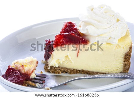 Fresh strawberry cheesecake with strawberry slices and whipped cream and a fork in it.
