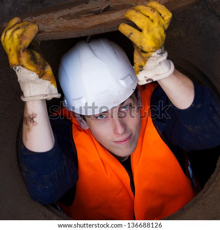 Worker holding manhole cover on top of his head while being half way inside the manhole / Down The Manhole