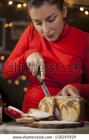 Beautiful Lady in red sweater cutting Christmas cake in the warmth of her home.