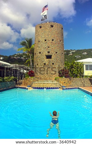 Girl is swimming in the clear blue pool located next to famous landmark of Blackbeard Pirate Tower on Caribbean  Island of St. Thomas
