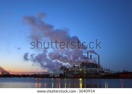 Paper factory pipers with the clouds of smoke in the nighttime sky reflected in the river.