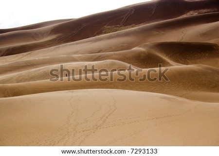 People small like ants walking far-away in dunes with sand being blown over by wind