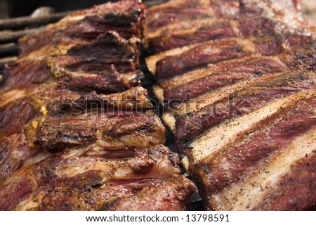 Two racks of grilled ribs are grilling on charcoal