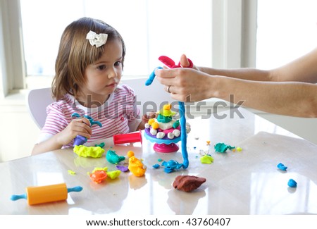 Hands of young woman show little girl how to use play dough