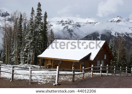 Simple log home with snow covered roof in mountain setting