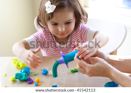 Hands of young woman show little girl how to use play dough