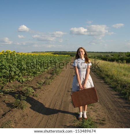 woman traveling with a suitcase in hand on the background of the rural roads and fields of sunflowers