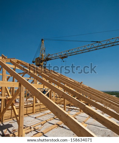 Construction worker working on the installation of a timber frame house roof and crane