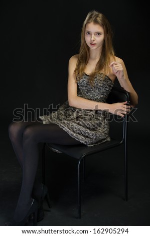 portrait of a beautiful young woman with her hair sitting on a chair on a black background