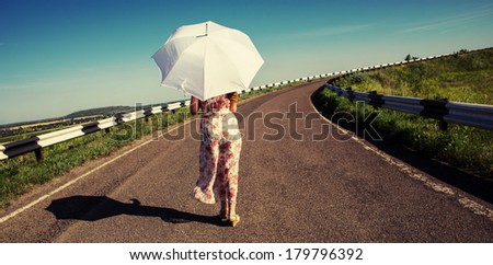 Girl with white umbrella walking along the road. Sunny day.