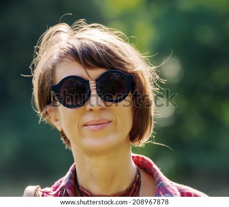 portrait of a pretty woman in sunglasses on background of city park, age forty to forty-five years