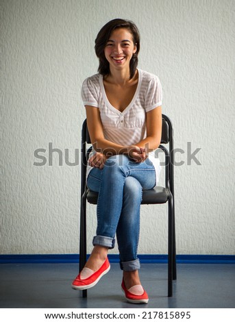 Chinese woman sitting on a chair and smiling on a background of bright wall
