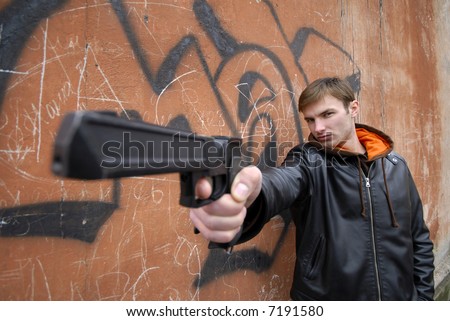 young guy with  pistol in  hand on  background of  wall