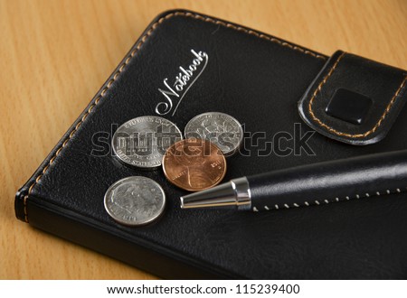 Black notebook, US coins and pen on the desk