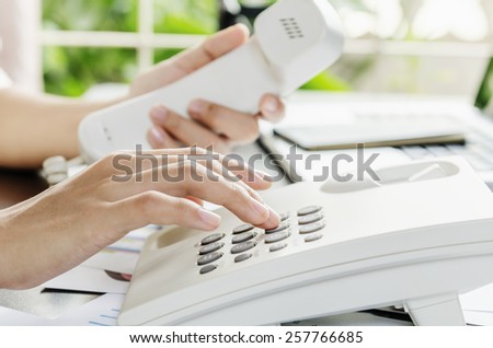 Woman dialing on a telephone in an office