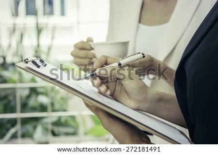 business people writing in a note pad and holding coffee cup