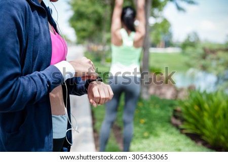 woman using smart watch and another woman stretching