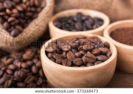Ground coffee and coffee beans in the wood bowls, background is the coffee bags on the wooden table