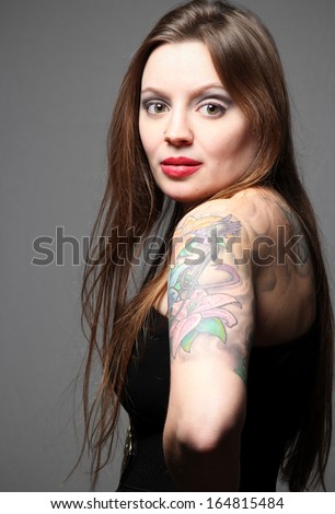 Beautiful hip female fashion model with long hair and tattoo sleeve, wearing black dress.