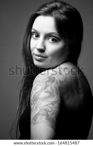 Black and white portrait of female fashion model with tattoo, looking over her shoulder.