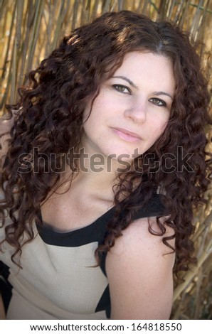 Beautiful brunette woman with curly brown hair poses in fields