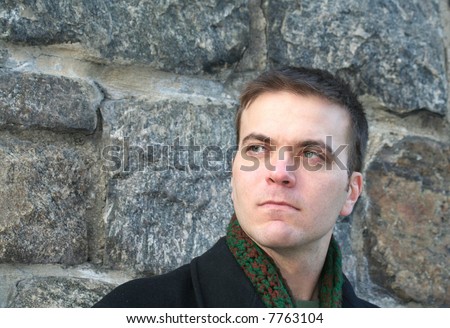 Green-eyed man leans against wall, waiting
