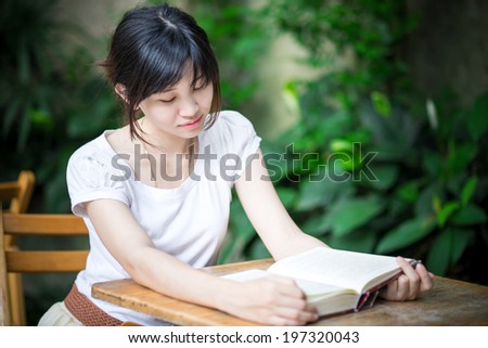 Young asian woman  sitting on a chair with ice coffee reading a book in garden
