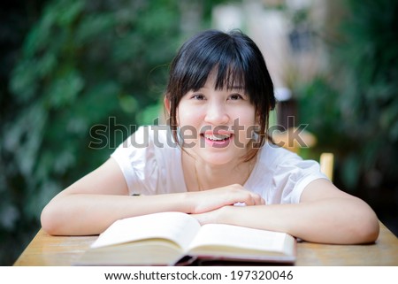 Happy asian woman sitting on a chair with ice coffee reading a book in garden