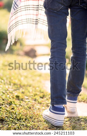 Young woman in blue jeans walking on green grass in sunset