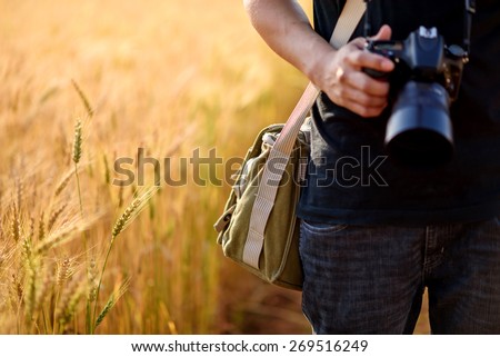Photographer holding camera on wheat fields in warm sunset