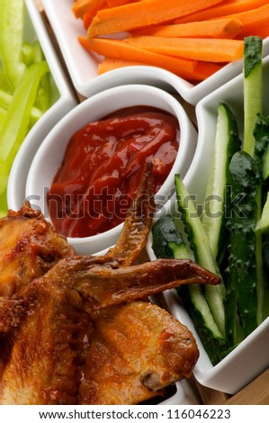 Chicken Wings and Snacks with Barbecue Sauce, Cucumber, Bell Pepper and Carrot Sticks closeup