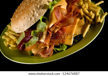 Big Tasty Burger with Grilled Bacon, Cheese, Lettuce, Ketchup and French Fries on Green Plate closeup on black background