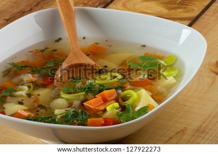 White Bowl of Vegetable Soup with Potato, Carrot, Bell Pepper, Leek, Parsley and Dill with Wooden Spoon closeup on Wooden background