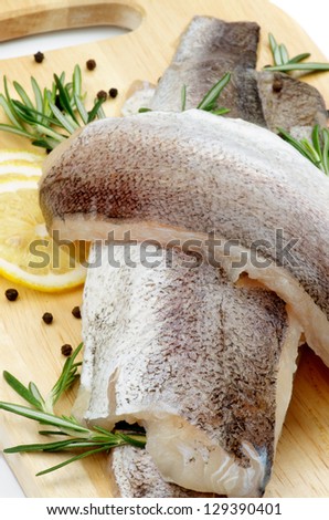 Heap of Raw Fish Hake Fillets with Lemon, Black Peppercorn and Rosemary closeup on Cutting Board