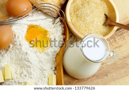 Preparing Dough. Ingredients with Jar of Milk, Flour, Butter, Eggs, Sugar and Wooden Spoon with Egg Whisk closeup on Wooden background. Top View