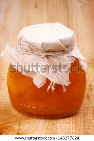 Glass Jar with Homemade Apricot Jam Covered Butter-Paper on Wooden background