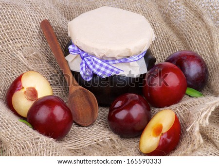 Arrangement of Jar of Plum Jam with Wooden Spoon,  Ripe Purple Plums Full Body and Halves closeup on Burlap background