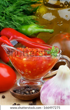Arrangement of Bruschetta Sauce in Glass Gravy Boat with Black Tomatoes, Garlic, Chili Peppers and Glass Bottle of Olive Oil closeup on Wooden background