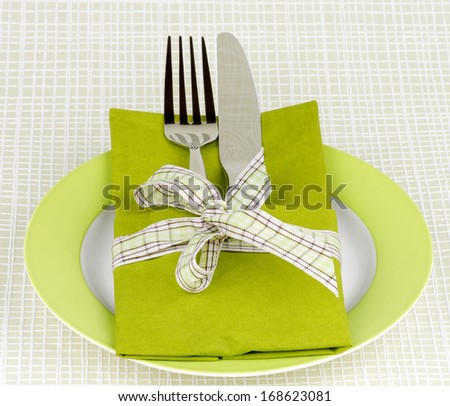 Elegant Table Setting with Fork and Table Knife into Green Napkin Decorated with Green Checkered Bow on Green Plate