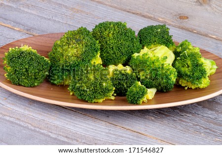 Wooden Plate with Crunchy Ready-to-Eat Boiled Broccoli isolated on Rustic Wood background