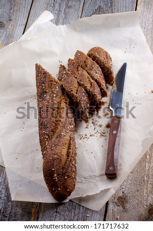 Half of Sesame and Poppy Seed Brown Bread and Slices with Table Knife on Parchment Paper closeup on Wooden background