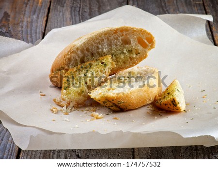 Crushed Slices of Garlic and Herbs Bread on Parchment Paper closeup on Rustic Wooden background