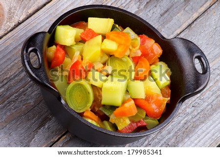 Vegetable Stew with Zucchini and Leek in Black Stew Pan closeup on Rustic Wooden background