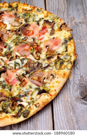 Part of Freshly Baked Pizza with Edible Mushrooms, Bacon, Cheese and Spinach Sauce on Rustic Wooden background