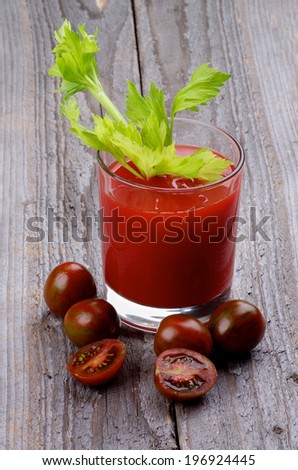 Brown Cherry Tomatoes Full Body and Halves with Glass of Freshly Squeezed Tomato Juice with Celery isolated on Wooden background
